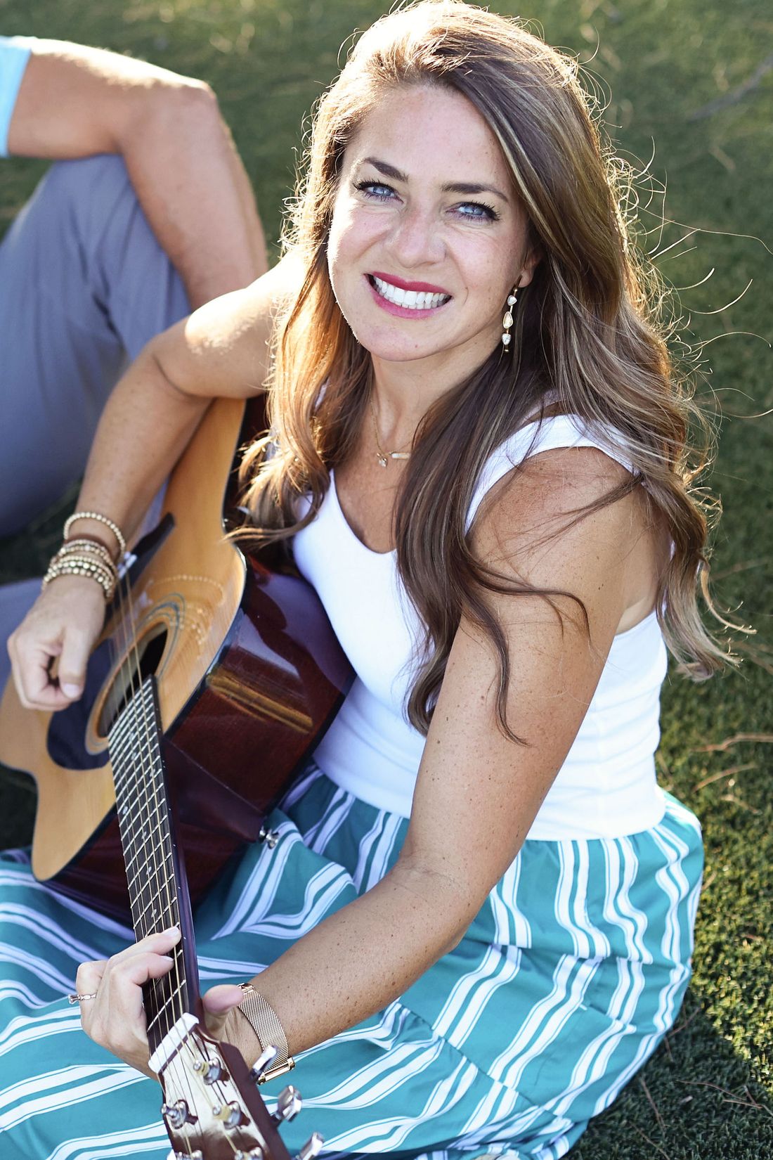Carrie Gotcher smiling, sitting in the grass with her guitar